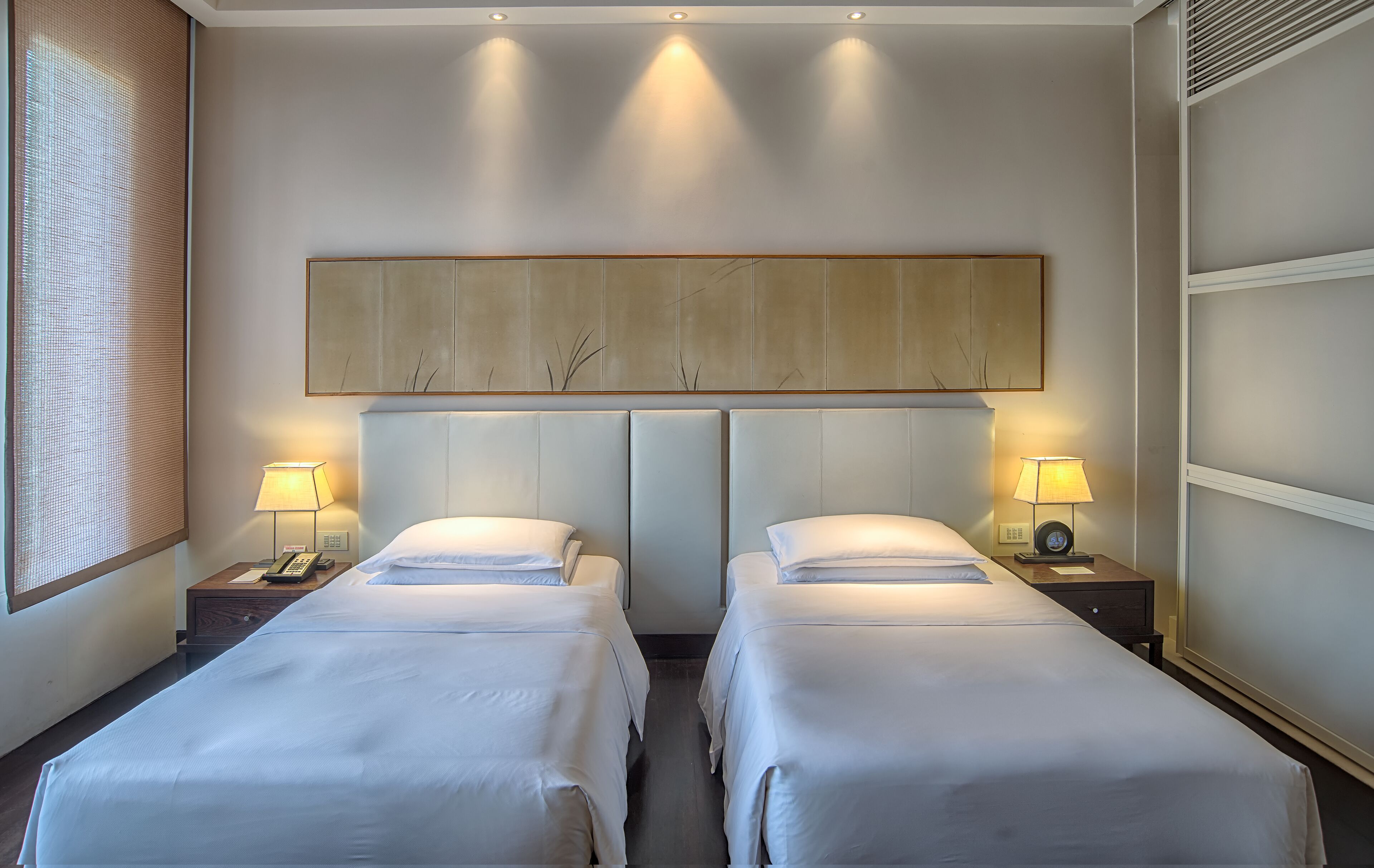 Habitación de hotel con dos camas, un cuadro grande sobre las camas y una ventana con persianas.