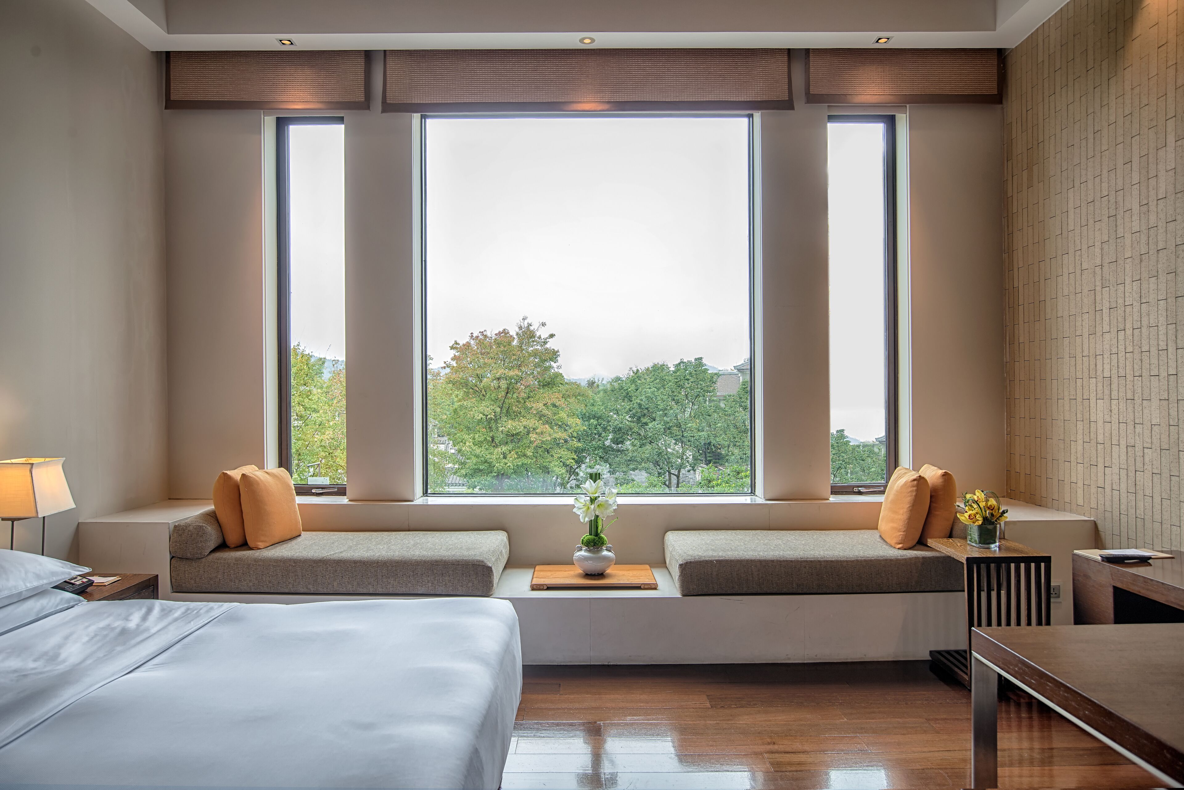 A hotel room with a large window, a sofa bed, a bedside table, and a bed.