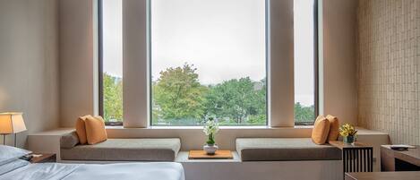 A hotel room with a large window, a sofa bed, a bedside table, and a bed.