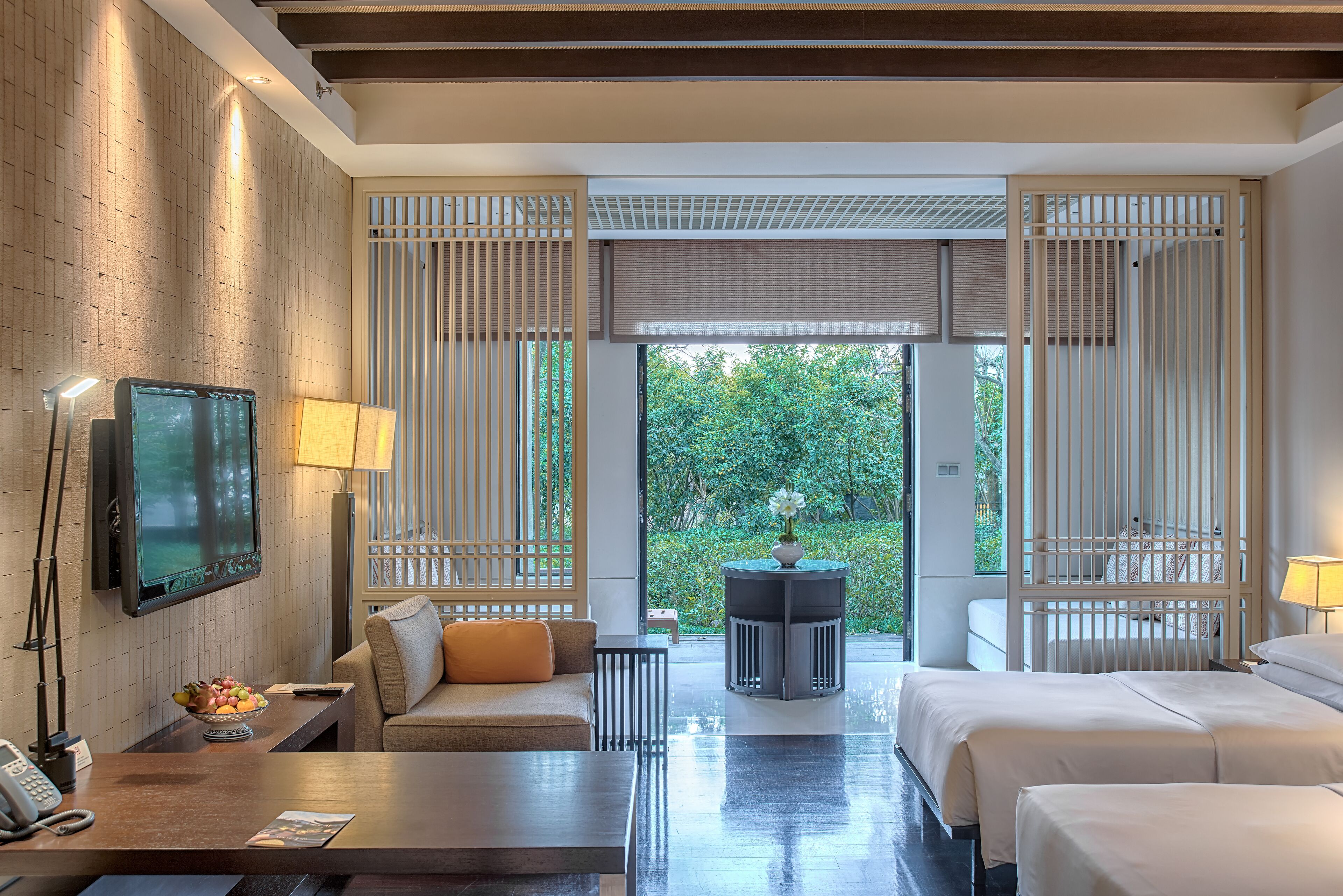 Una habitación de hotel moderna con una pared de madera, televisión, sofá, mesa de comedor y cama.