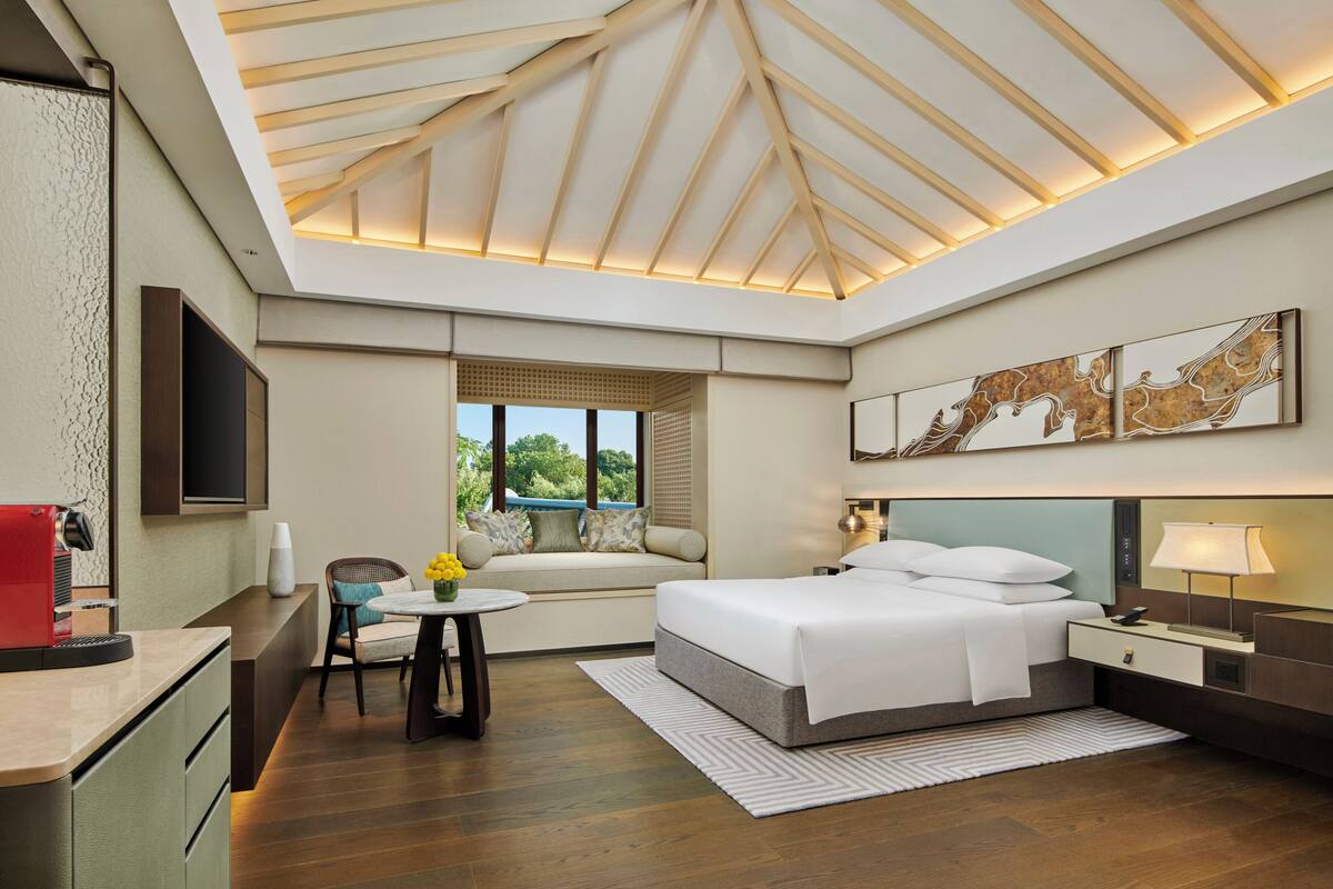 Une chambre d’hôtel moderne, dotée d’un grand lit, d’un bureau, d’une chaise et d’une fenêtre donnant sur un paysage verdoyant.