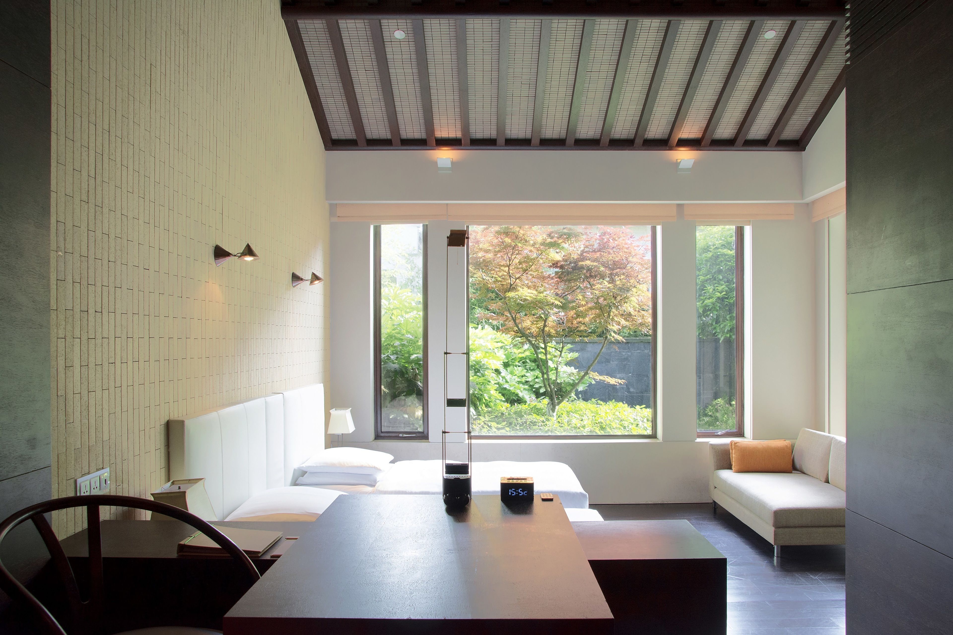 Ein modernes Hotelzimmer mit einem großen Bett, einem Schreibtisch und einer Couch. Große Fenster bieten Blick ins Freie.