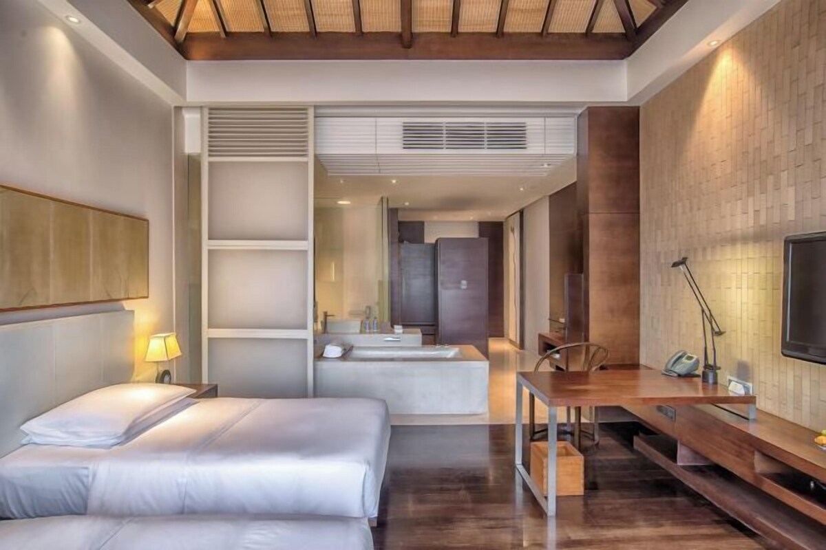 Quarto de hotel moderno com cama, escrivaninha, televisão e banheiro.