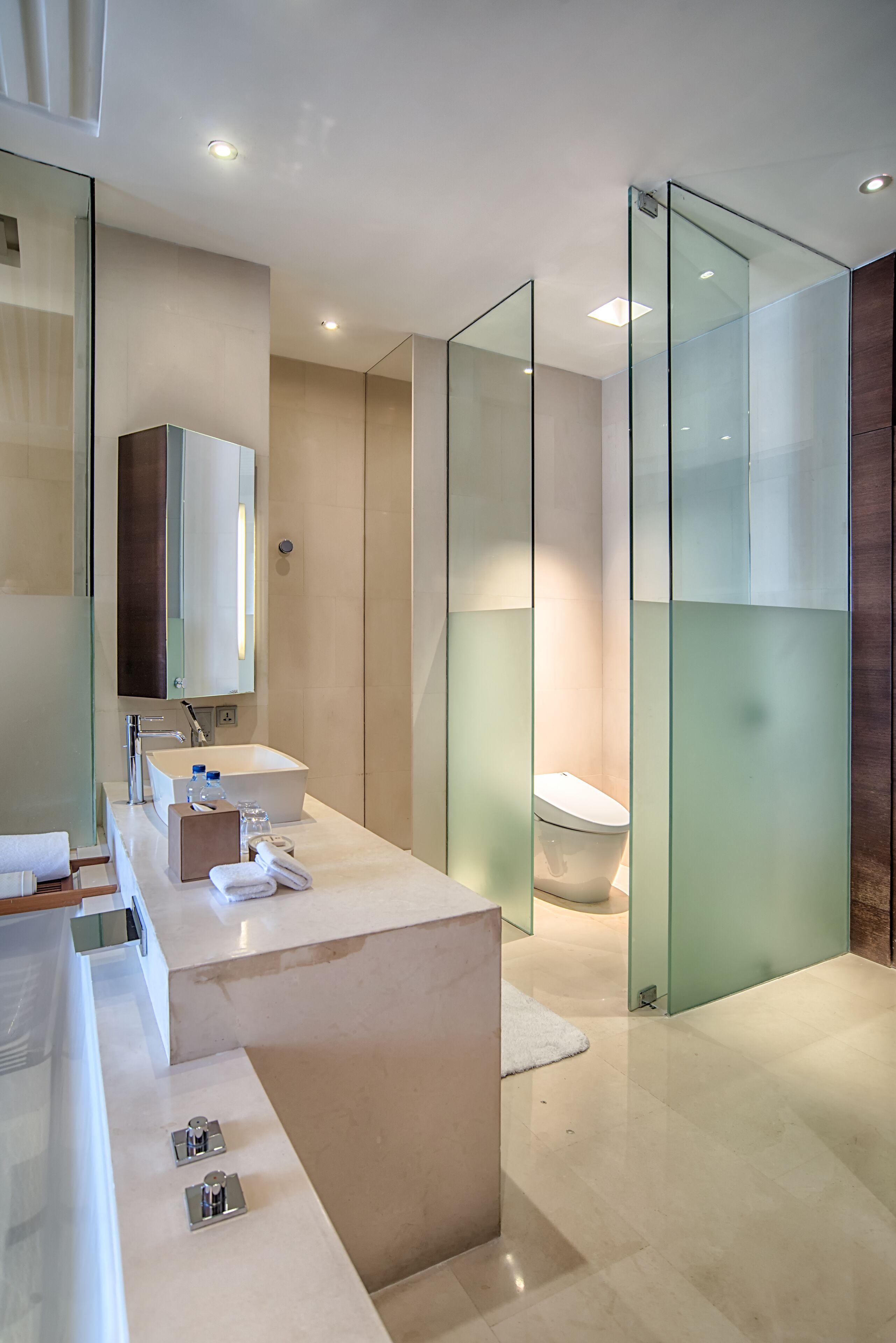 A modern bathroom with a glass partition, a large mirror, a white sink, and a toilet.