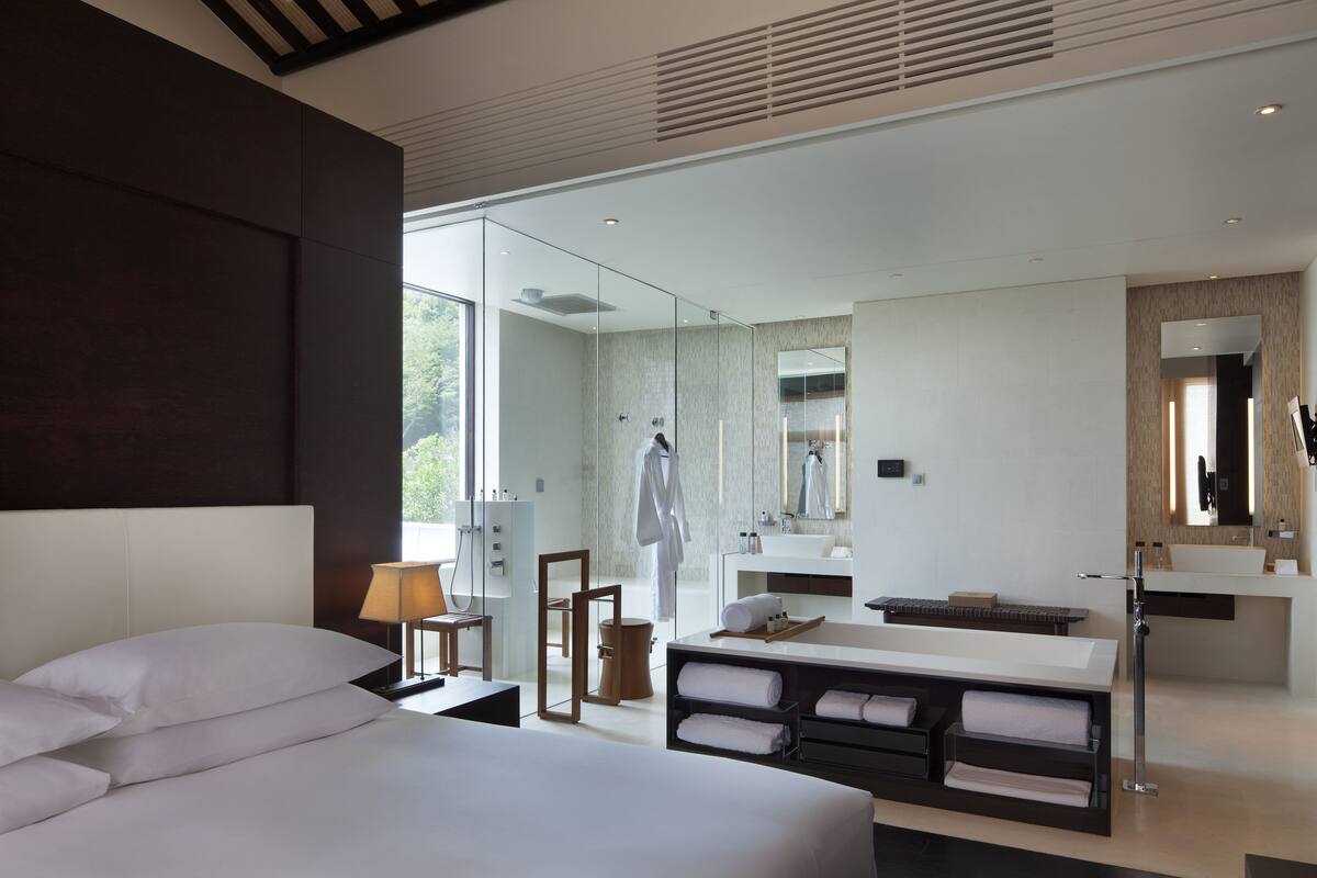 Une chambre d’hôtel moderne dotée d’un grand lit, d’un coin salon, d’une salle de bain avec un grand miroir et d’une vue sur l’extérieur.