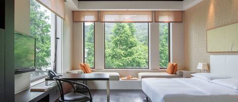 A modern hotel room with a large window, a bed, a desk, and a chair.