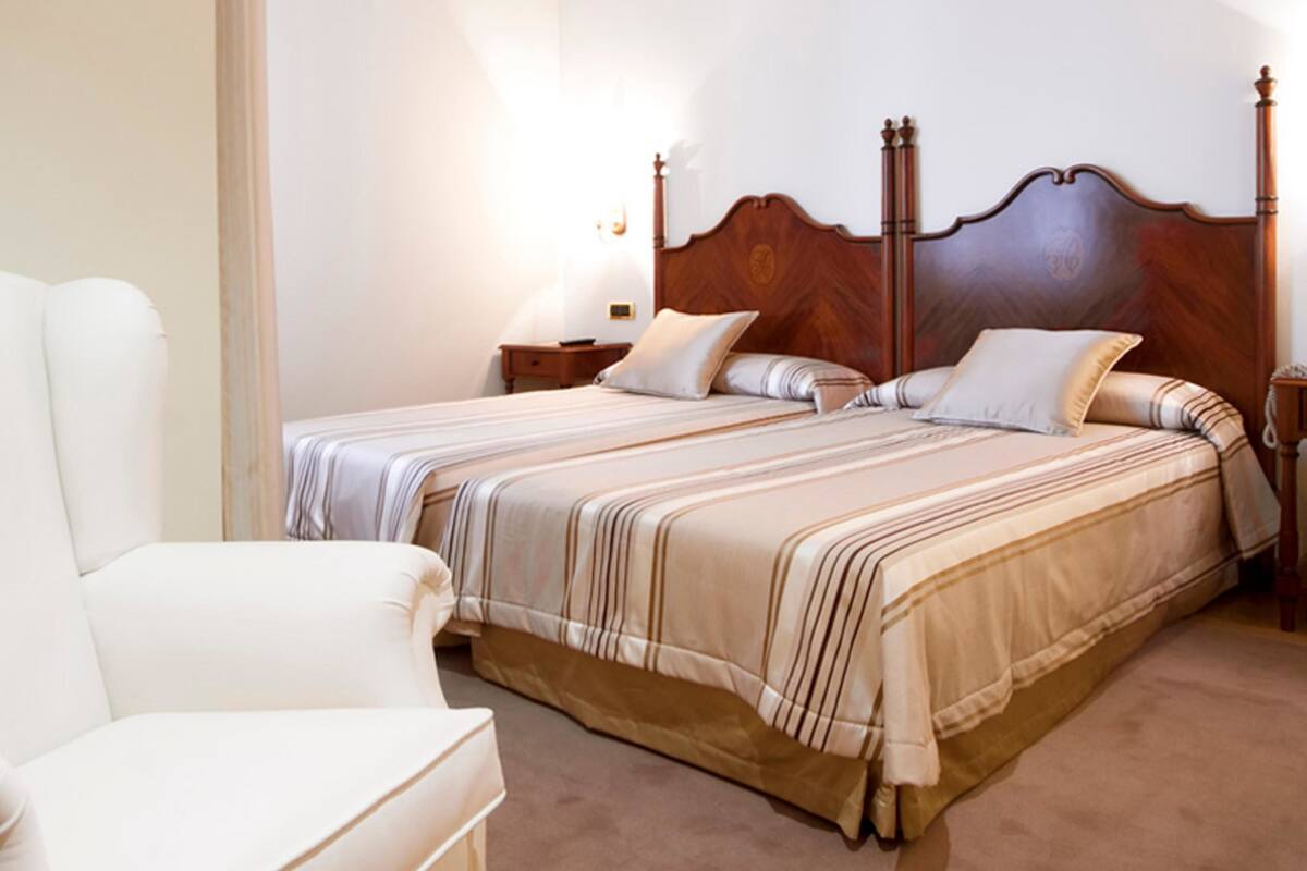 Un dormitorio con dos camas, un sillón blanco y un cabecero de madera.