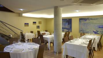 A dining area with round tables set for service, a central pillar, and a staircase.
