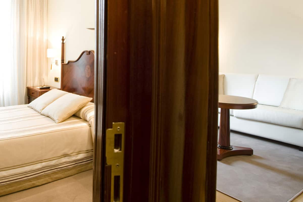 Una habitación de hotel con una cama, una puerta de madera, una mesita de noche, una lámpara y un sofá.