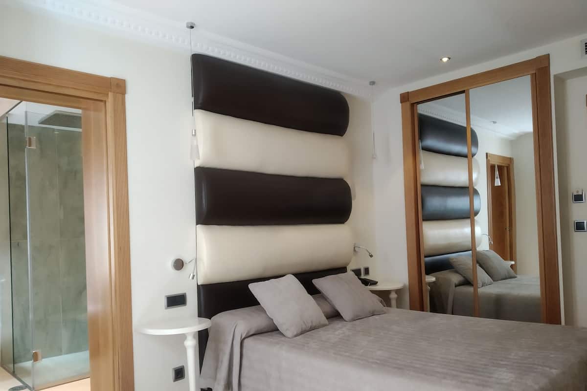 Un dormitorio moderno con una cama grande, una mesita de noche, un espejo y una cabina de ducha de vidrio.