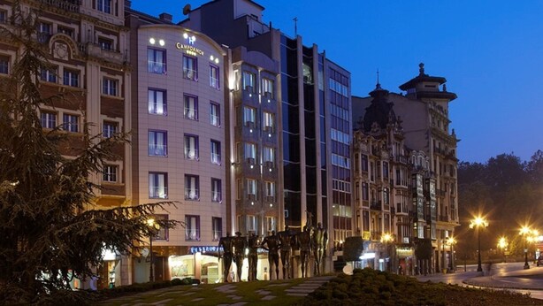 Un hotel con varios pisos, ventanas amplias y un área de entrada bien iluminada.