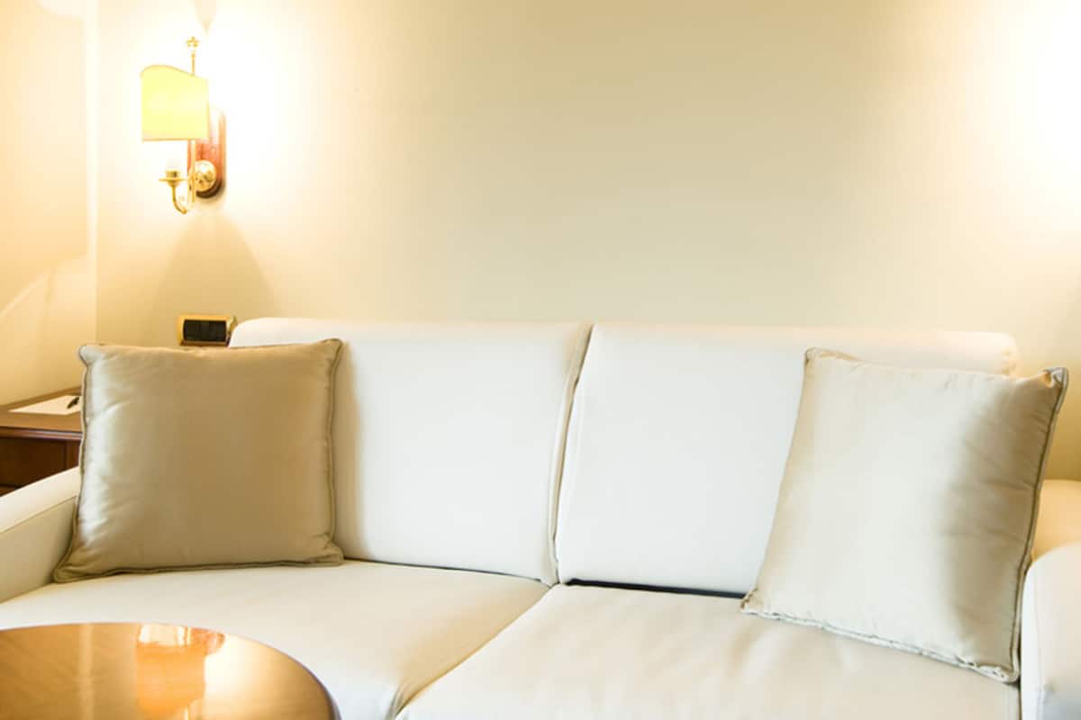 Un sofá blanco con tres cojines, una mesita redonda y una lámpara de pared.