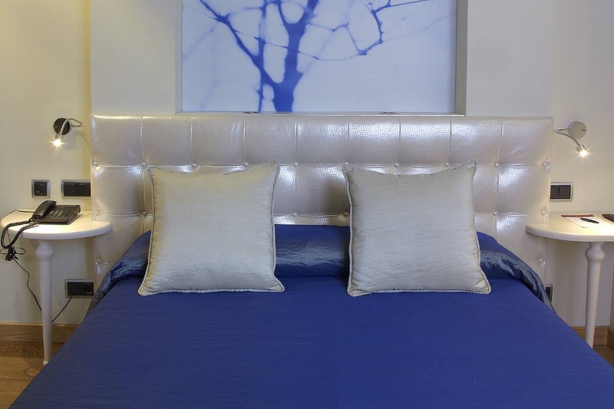 Un dormitorio con una cama grande, dos mesitas de noche, una obra de arte en la pared y un cabecero moderno.