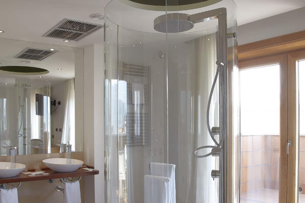 Un baño moderno con ducha envuelta en vidrio, tocador de madera con dos lavamanos y un espejo grande.