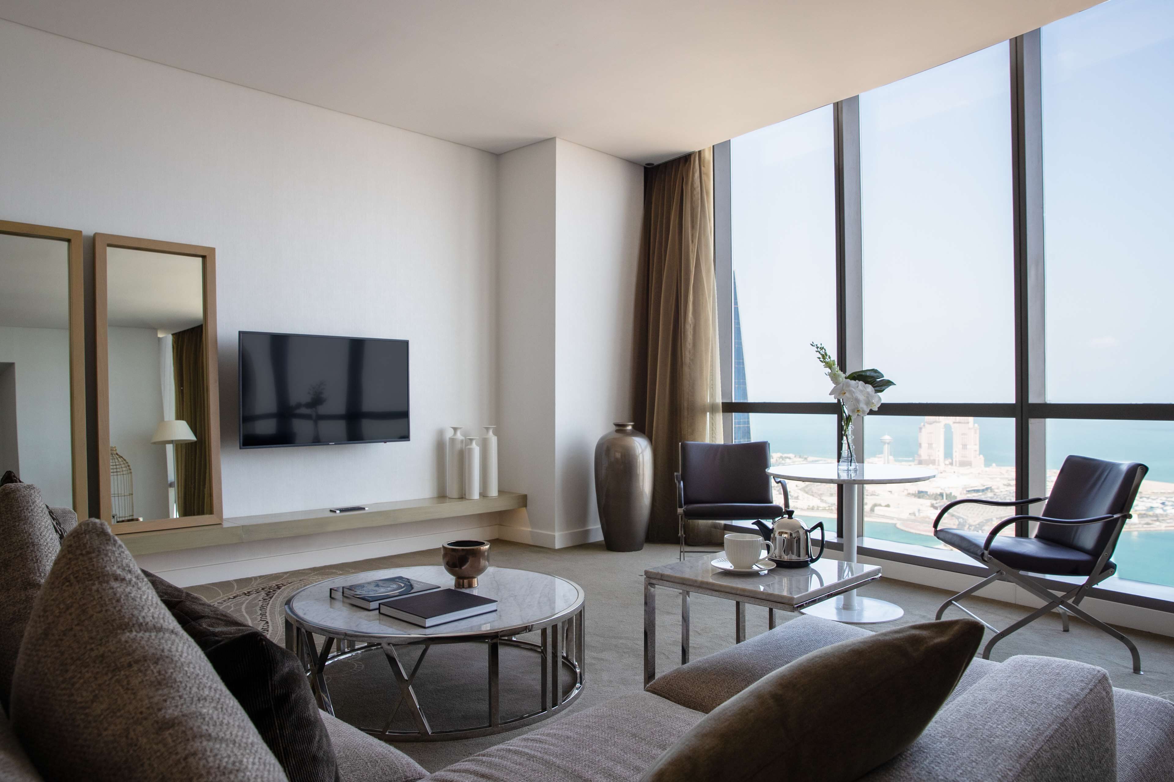 Een moderne hotelkamer met een groot raam dat uitzicht biedt op de stad, een flatscreen-tv, een ronde salontafel en een comfortabele zithoek.