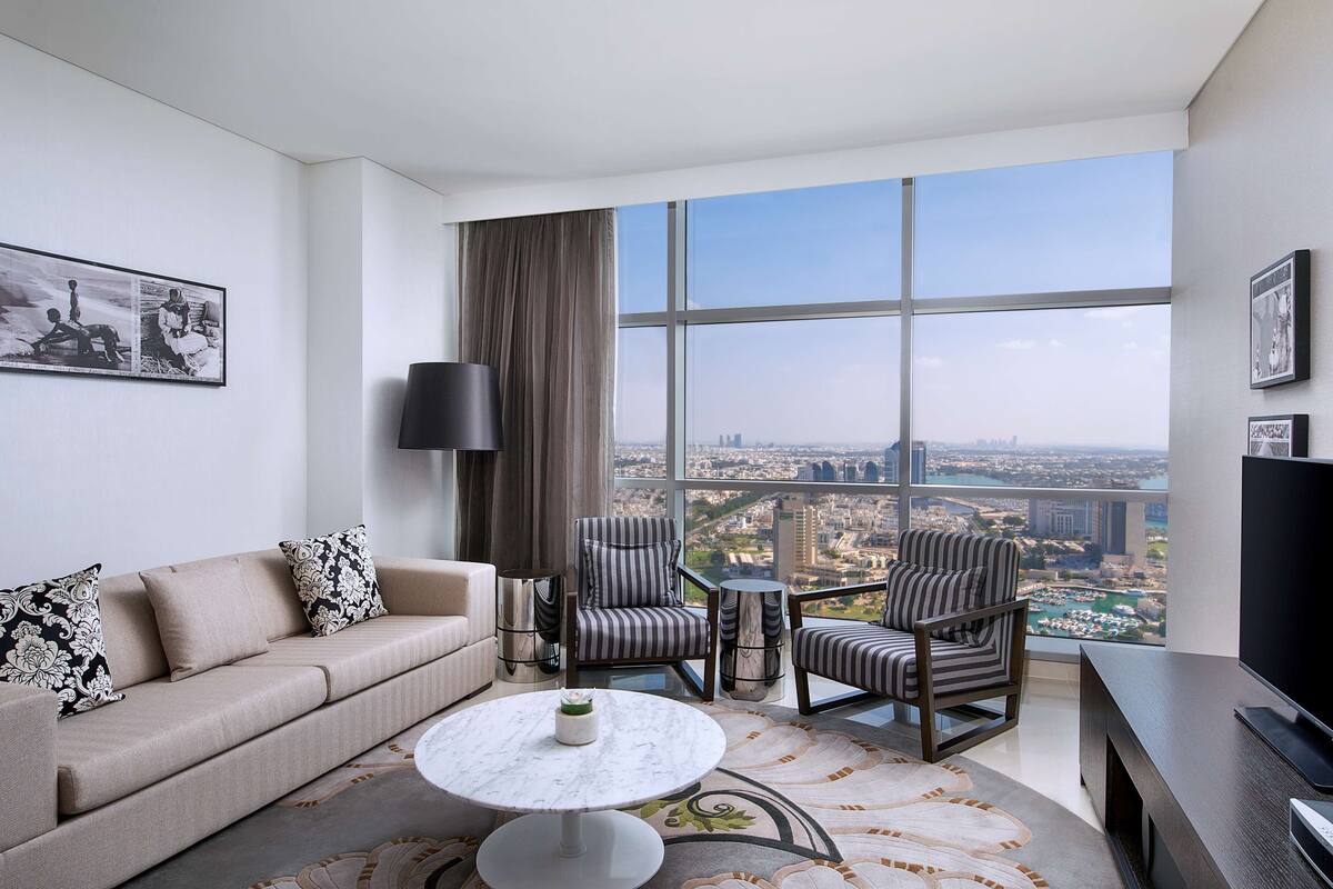Una sala de estar moderna con un sofá, sillones, una mesa de centro y un ventanal con vistas a la ciudad.