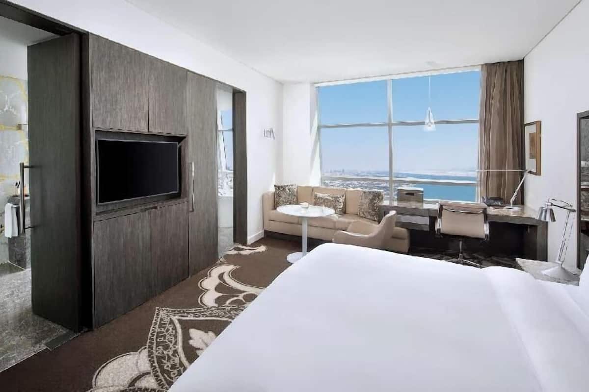 Habitación de hotel con una cama grande, televisión, sofá, una mesita y vista al océano.
