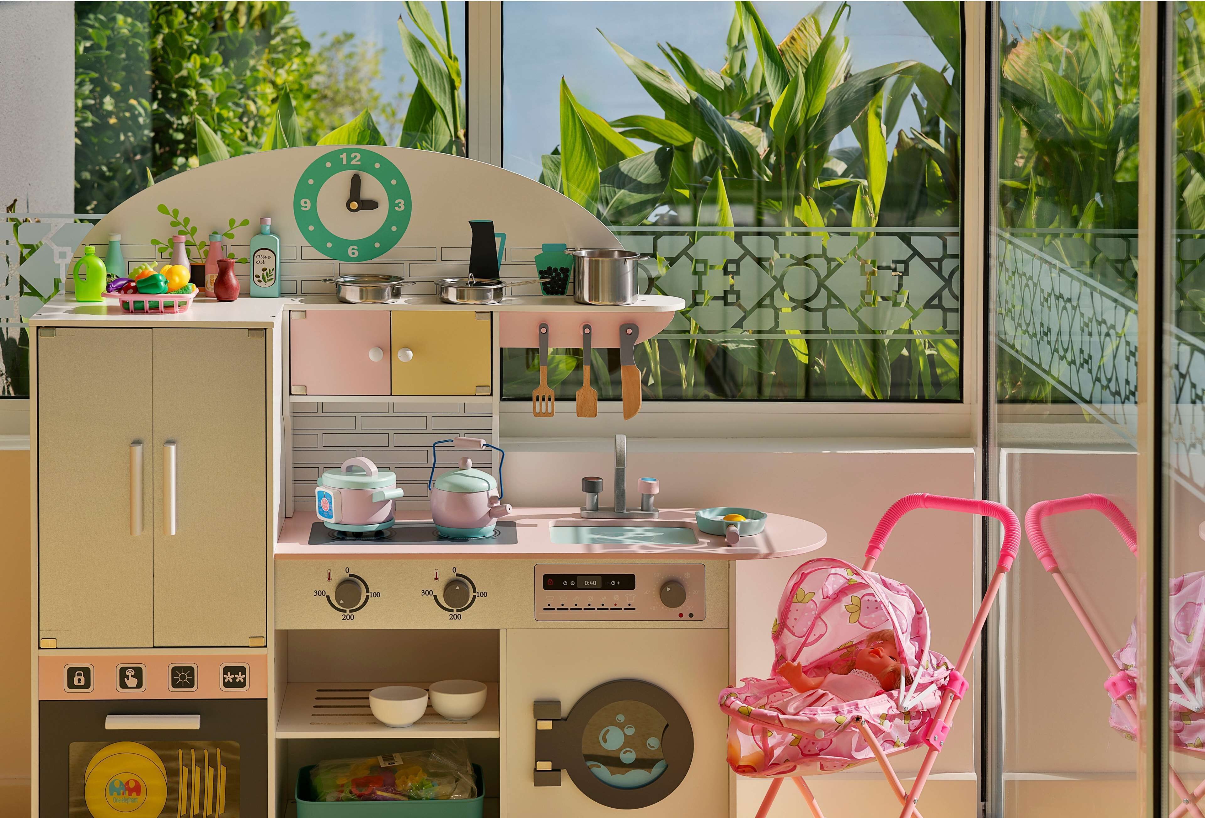 A children's play kitchen with a clock, utensils, and a toy baby carriage.
