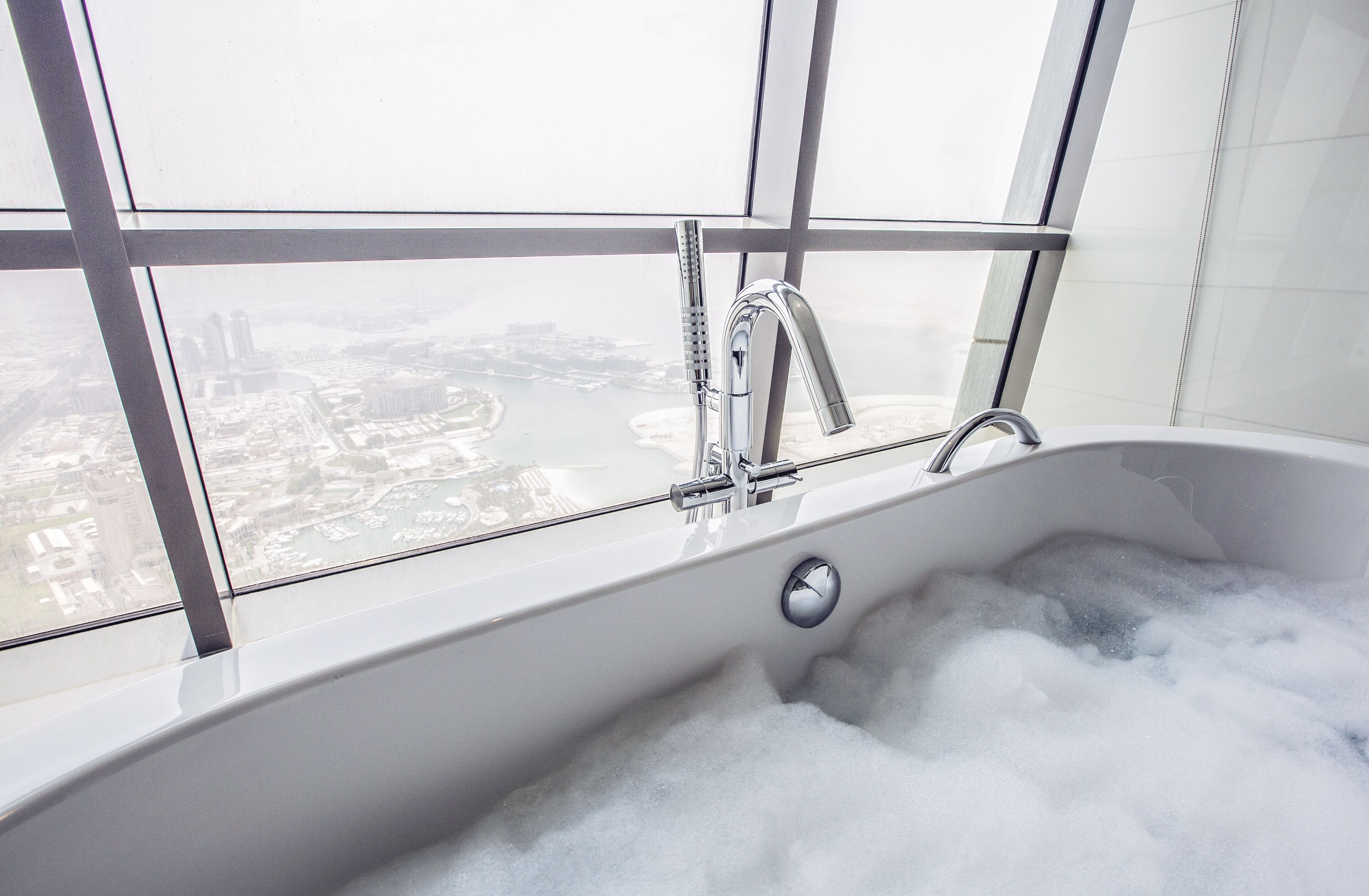 A bathtub with a view of a cityscape through a large window.