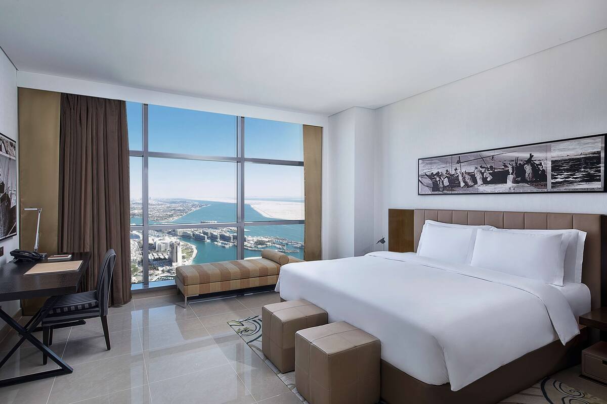 Habitación de hotel con un ventanal grande, una cama, un escritorio y una silla.