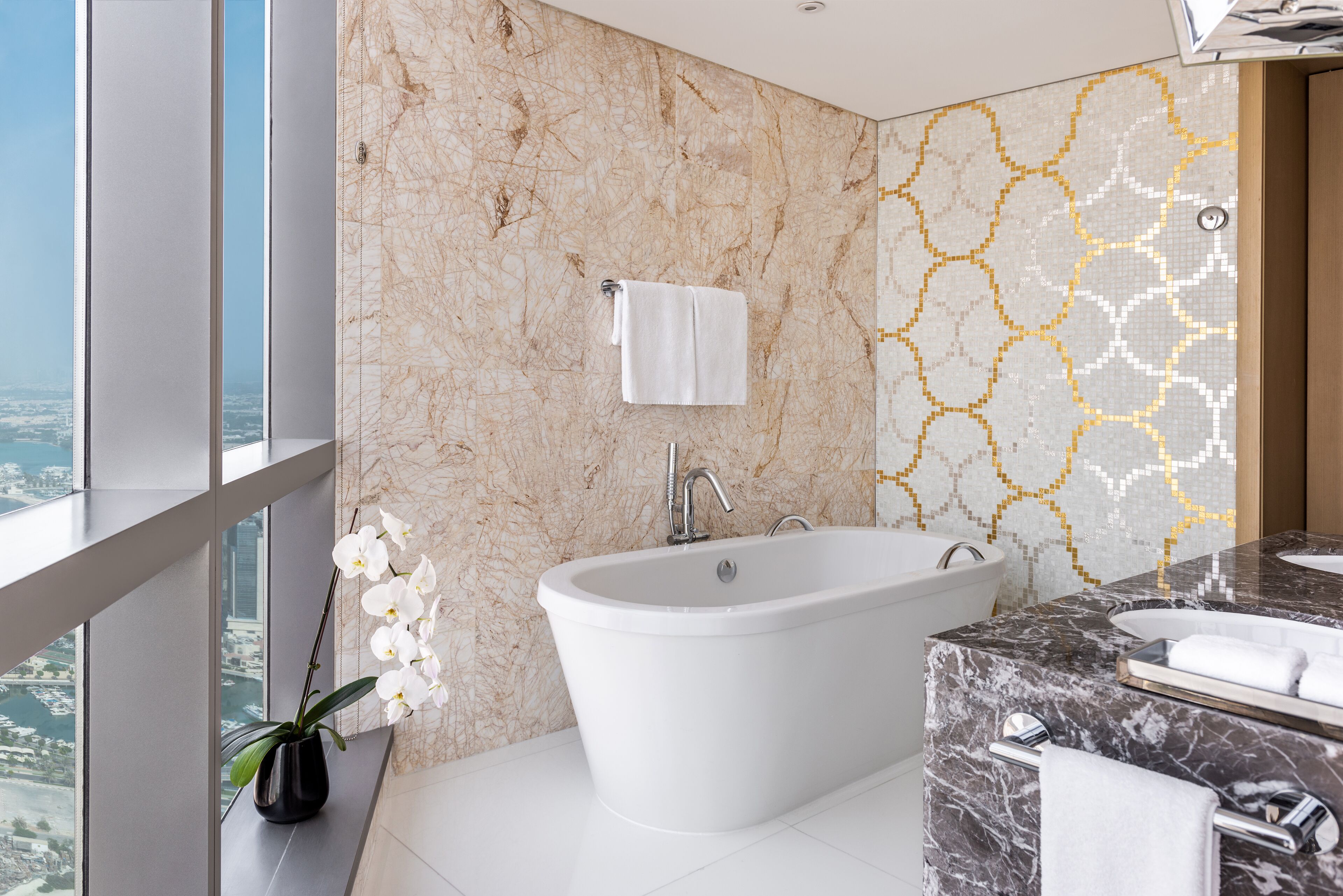 A modern bathroom with a freestanding bathtub, a marble vanity, and a large window offering a city view.