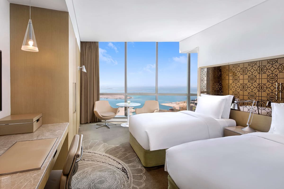 Una habitación de hotel con un ventanal grande, dos camas, un escritorio y una mesita.