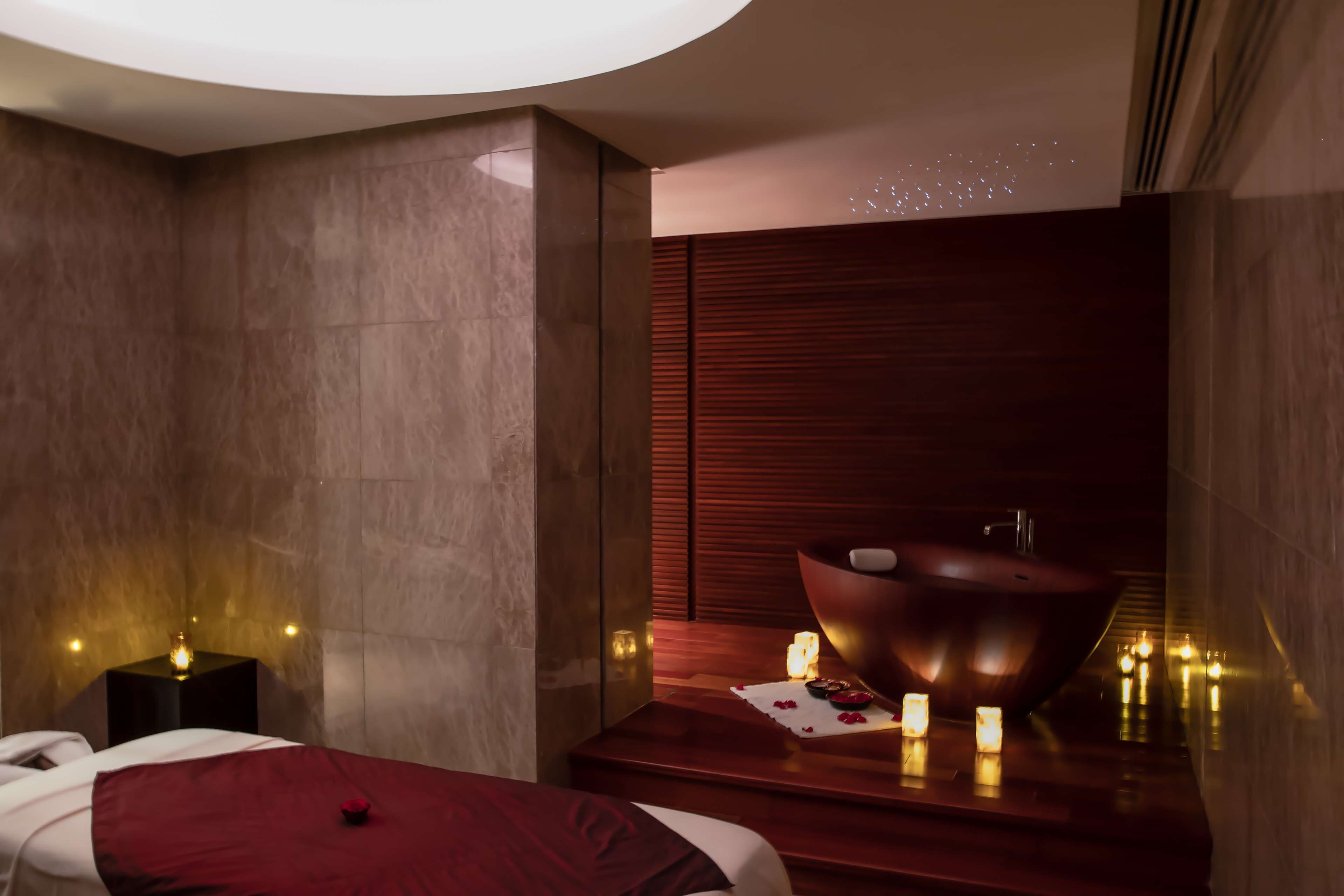 A modern spa room with a massage area, a wooden basin, and candles.