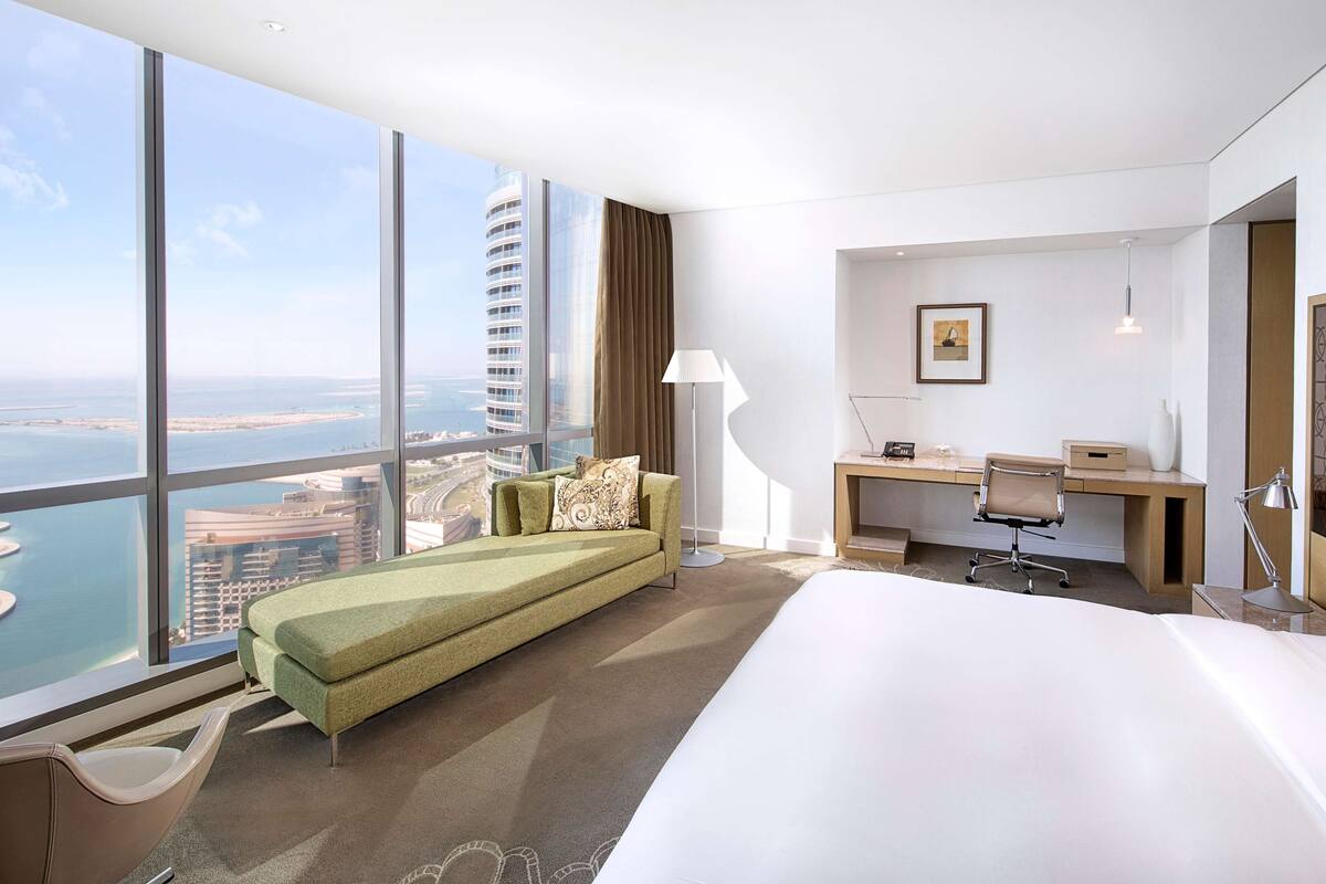 Habitación de hotel con una cama grande, un escritorio, una silla, un sofá y vistas a la ciudad y al agua.