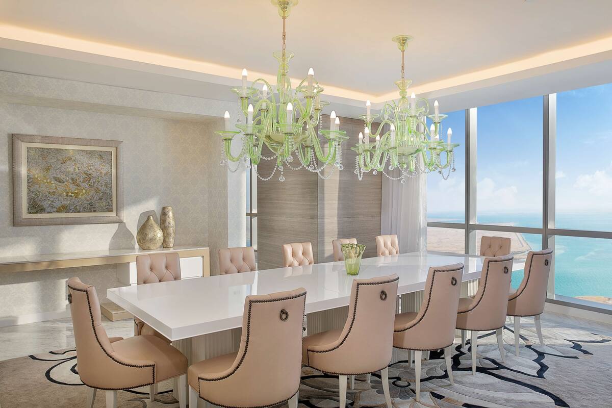 Un comedor moderno con una gran mesa blanca, seis sillas beige tapizadas y una lámpara de techo verde.
