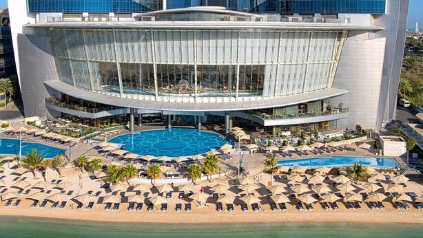 A modern hotel with a large pool area, multiple lounge chairs, and a view of the ocean. - Conrad Abu Dhabi Etihad Towers (Abu Dhabi)
