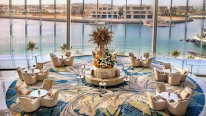 A luxurious lounge area with a central floral arrangement, surrounded by seating and a patterned floor, overlooking a body of water and buildings. - Conrad Abu Dhabi Etihad Towers (Abu Dhabi)