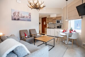 A modern living room with a sofa, chairs, a coffee table, and a dining area with a table and chairs. There is a kitchen in the background with cabinets and a microwave.