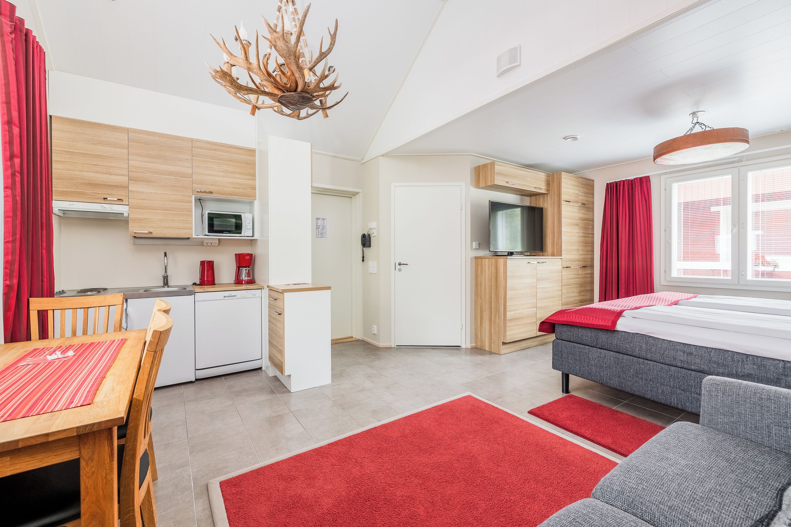 A modern kitchen with wooden cabinets, a microwave, and a coffee machine. There is a dining area with a table and chairs, and a sofa in the living area.
