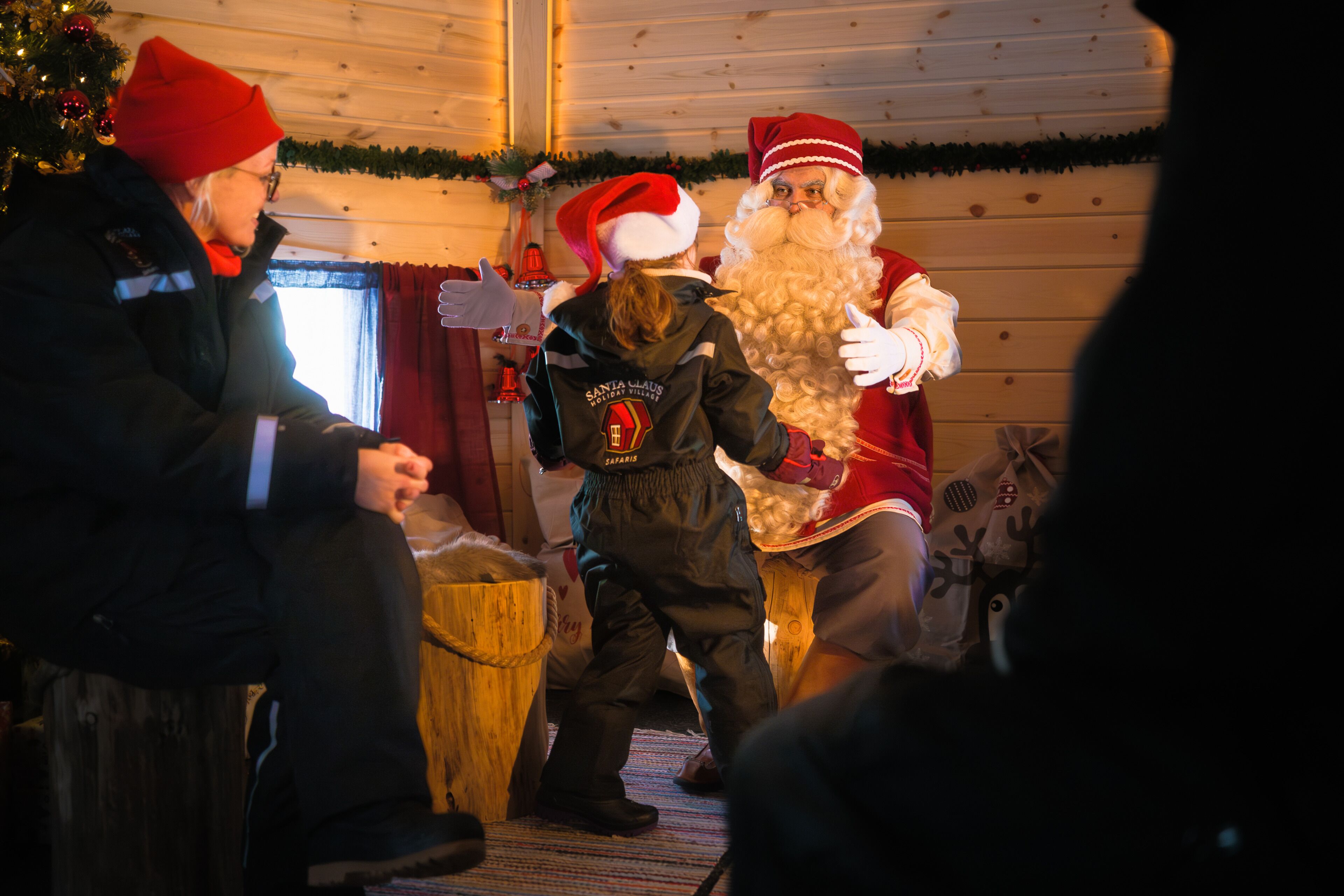 A room with wooden walls, a Christmas tree, and a person in Santa costume.