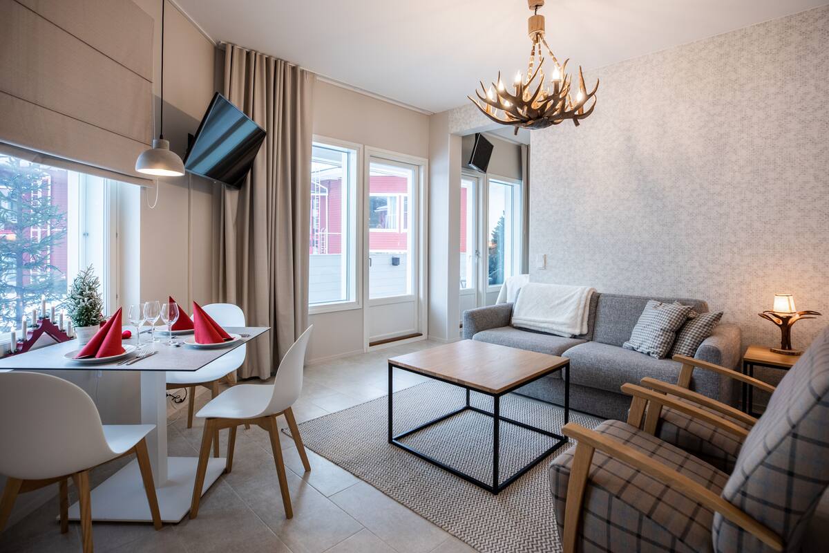 A modern living room with a sofa, a dining table set for two, a coffee table, and a chandelier.