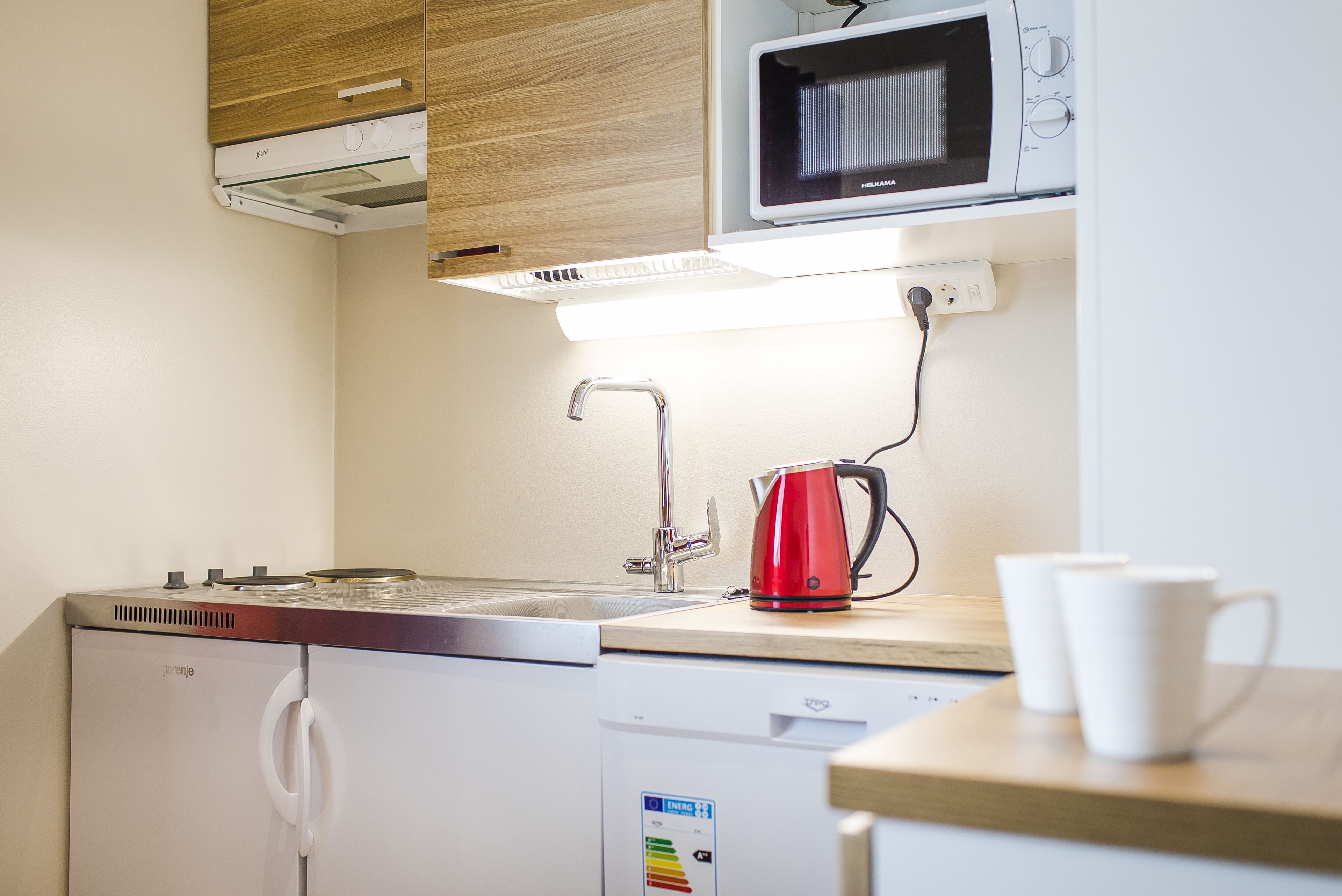 Una cucina compatta con forno a microonde, bollitore e macchina da caffè sul piano di lavoro.