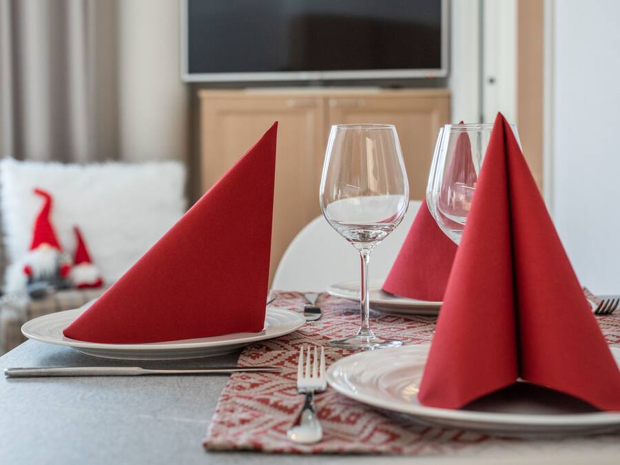 A dining table set with red napkins, wine glasses, and plates, with a patterned placemat and a fork on the table.