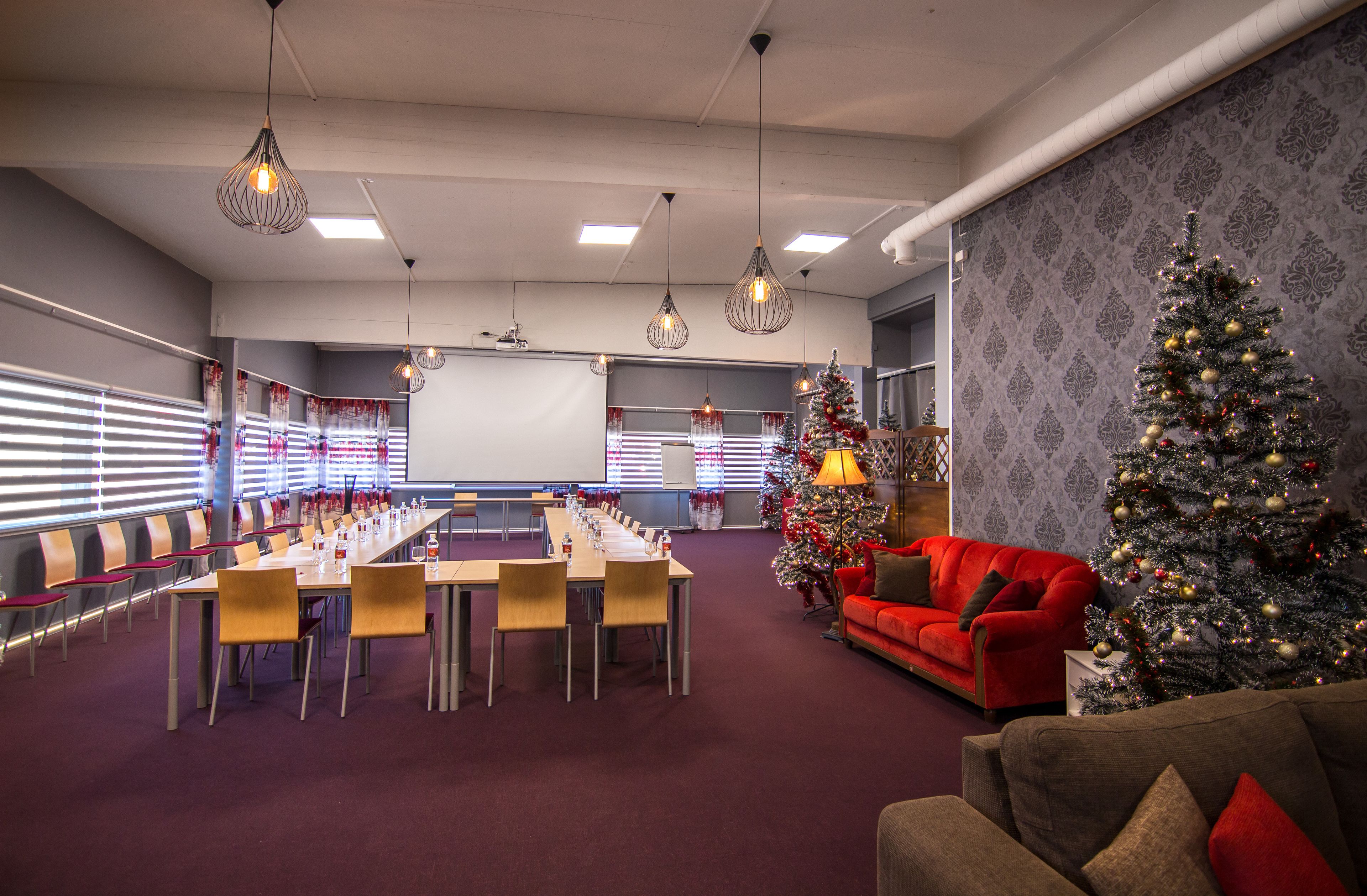 Una sala conferenze con un lungo tavolo, sedie e un divano rosso. Sono presenti due alberi di Natale addobbati con luci e decorazioni.