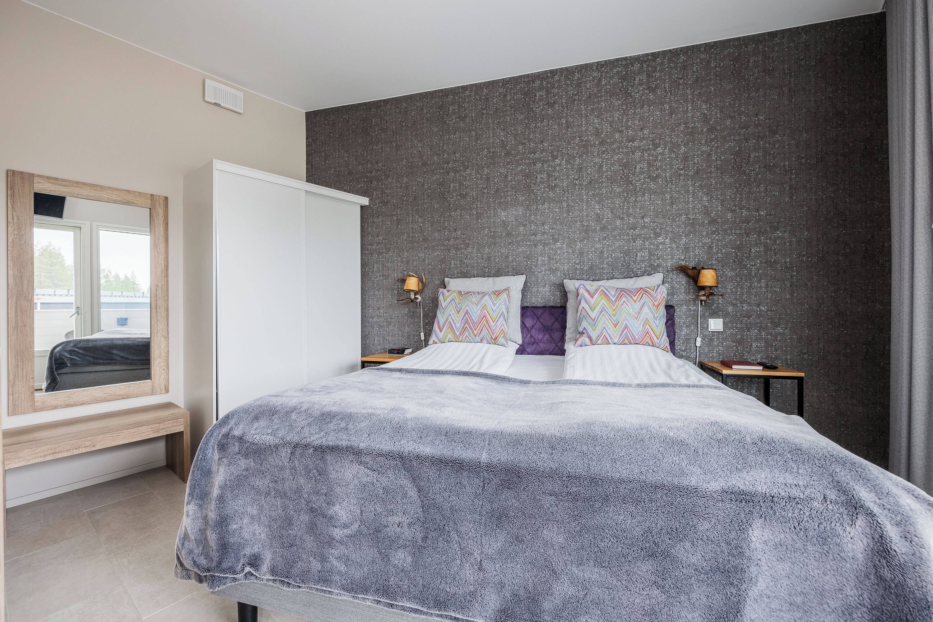 Une chambre à coucher avec un lit, des tables de chevet, un miroir et une fenêtre.