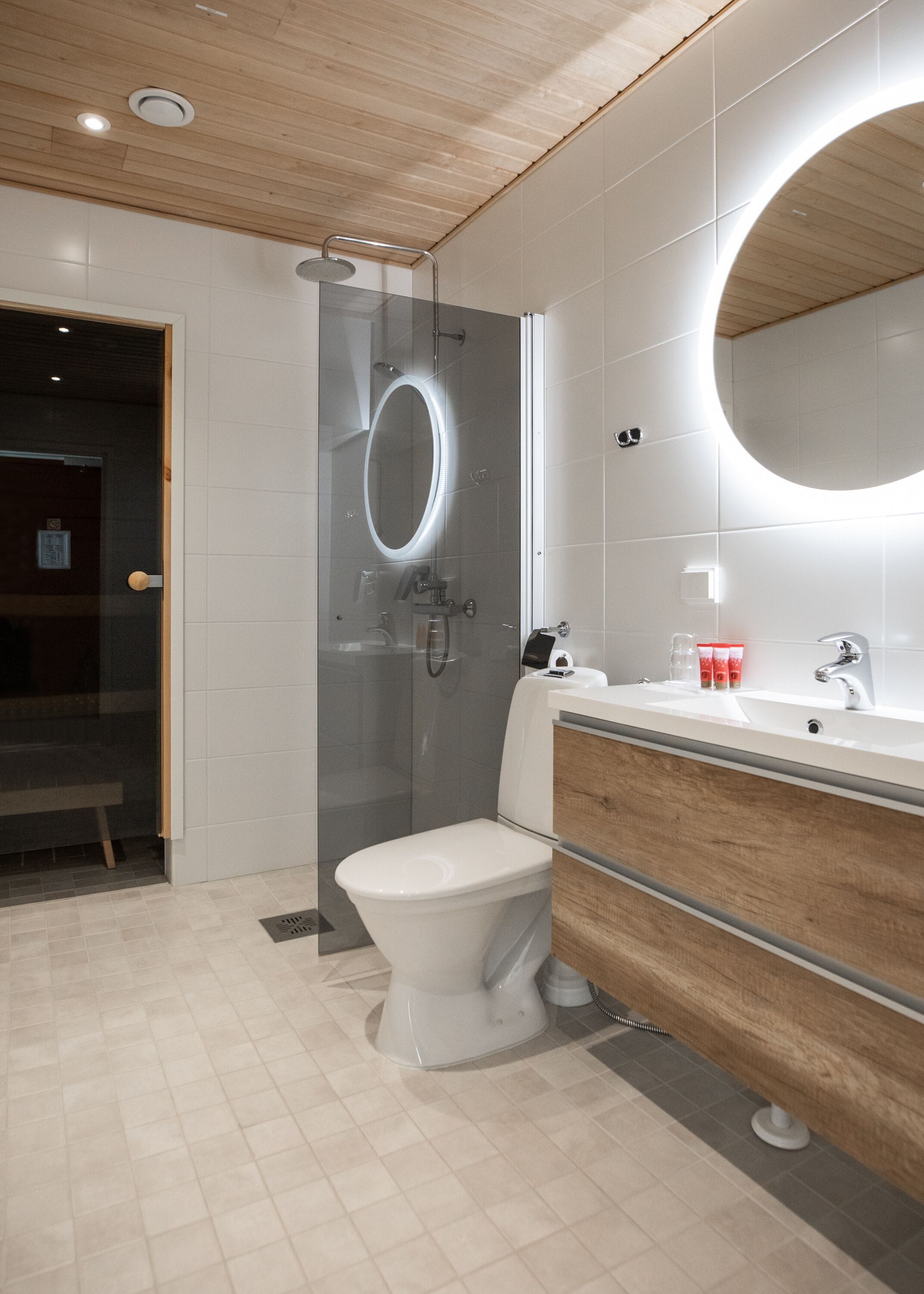 A modern bathroom with a glass-enclosed shower, a white toilet, a wooden vanity, and a large mirror.
