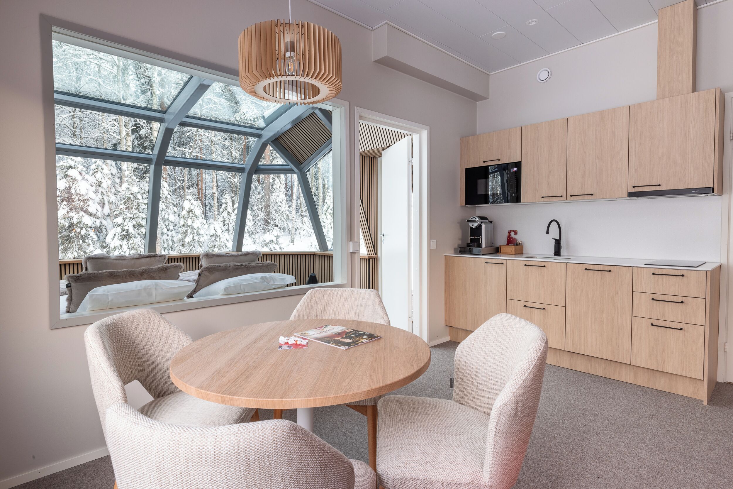 Une cuisine moderne avec des meubles en bois, une table à manger ronde et une grande fenêtre donnant sur des arbres couverts de neige.