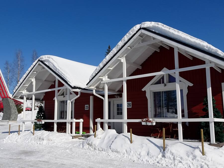 A red cabin with a snow-covered roof and white trim, surrounded by snow.