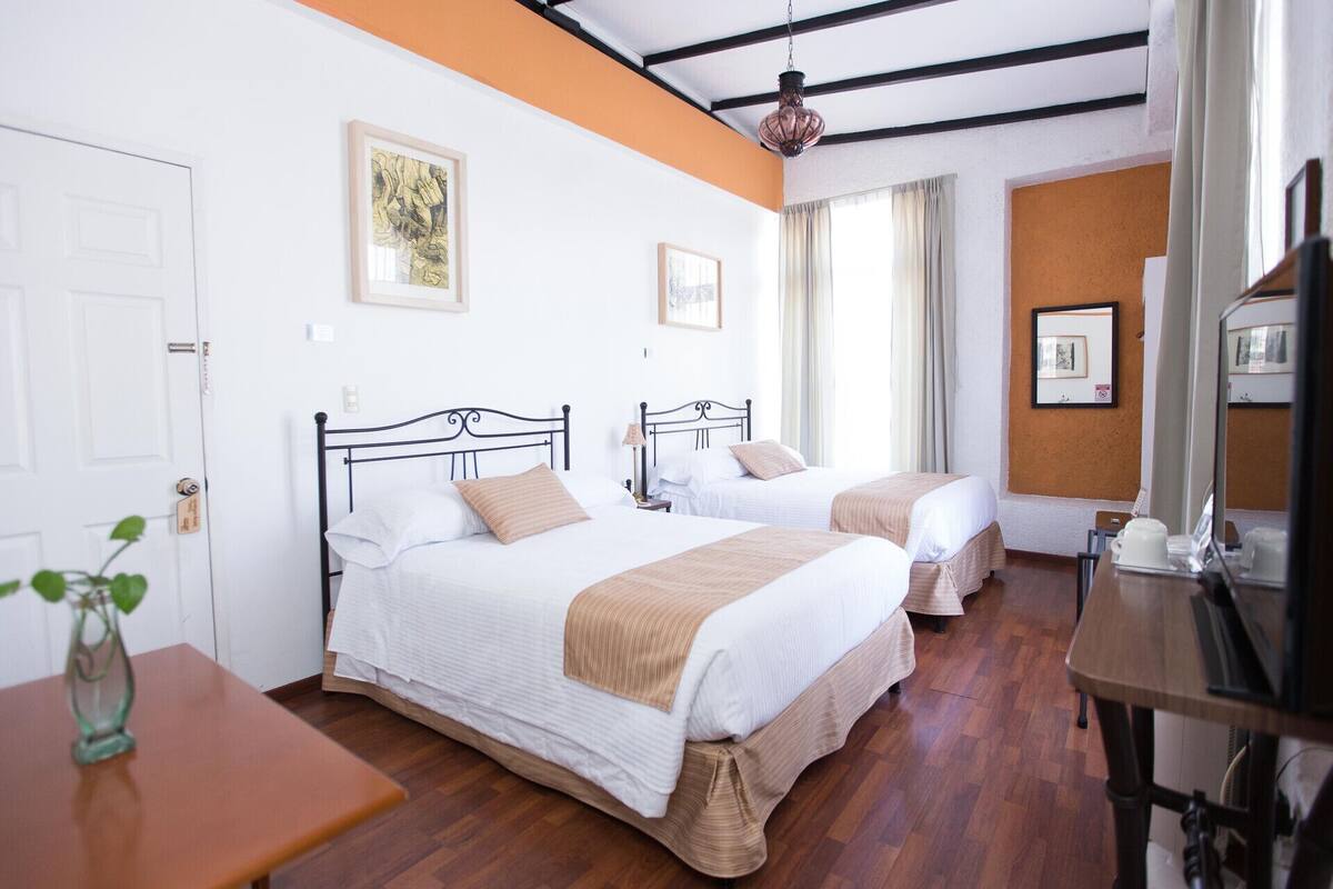 Une chambre d’hôtel avec deux lits, un bureau en bois, une petite table et un miroir.