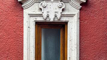 A window with ornate white trim and a wooden frame, set in a textured red wall.