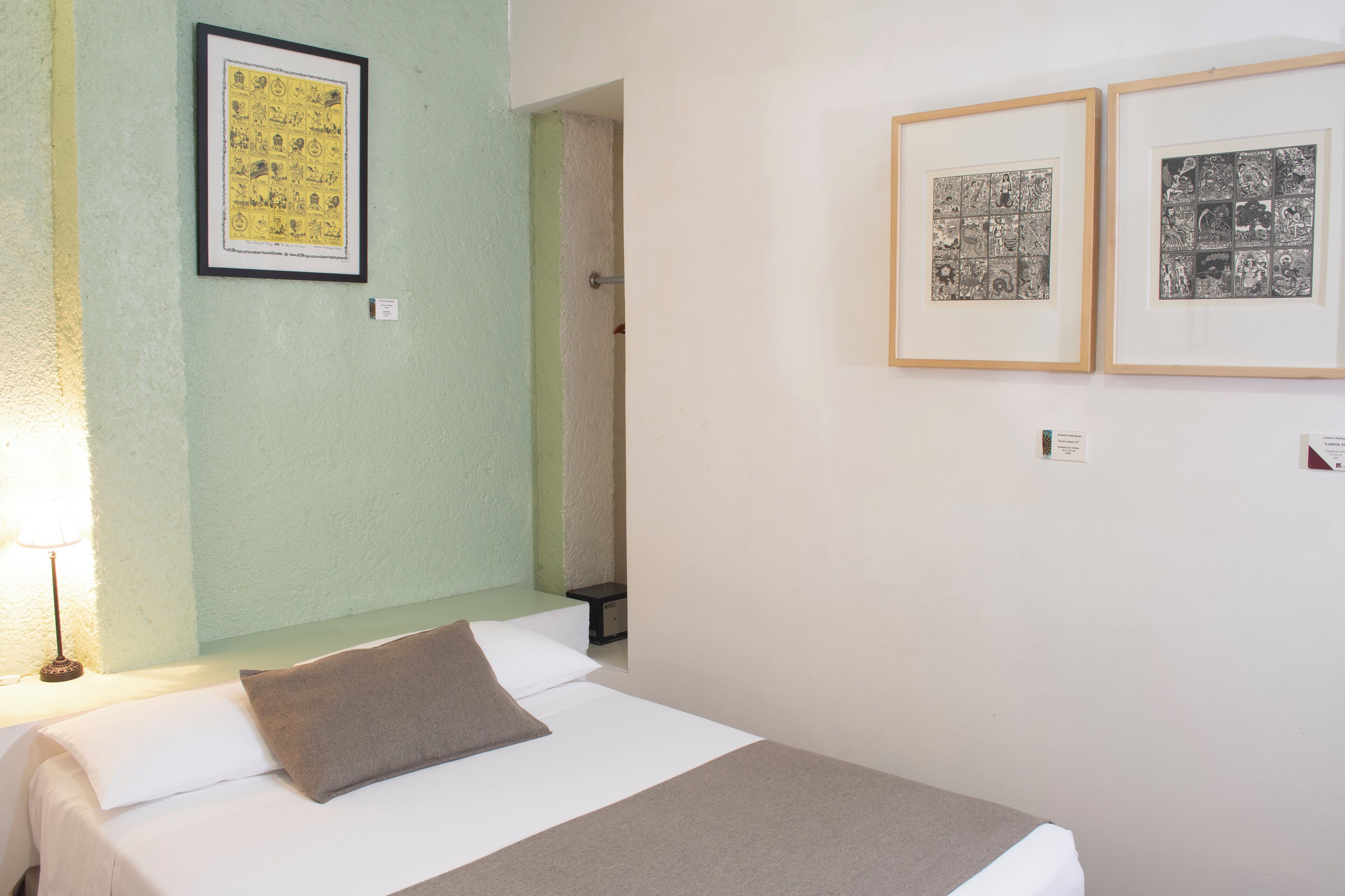 A hotel room with a bed, a nightstand, and two framed pictures on the wall.