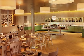 A restaurant with multiple dining tables and chairs, a central serving area, and green cabinets.