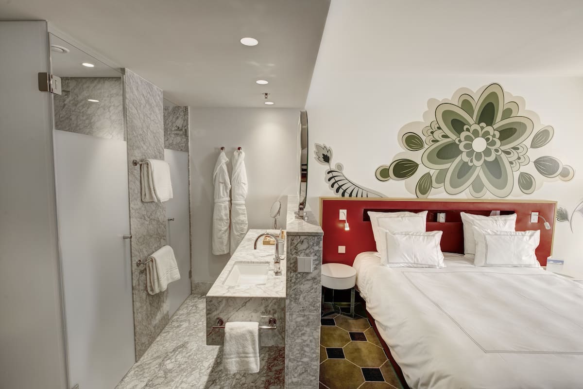 Een moderne hotelkamer met een marmeren badkamer, een bed met wit beddengoed en een decoratief behang.