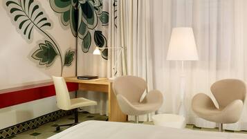 A hotel room with a bed, a desk, two chairs, a lamp, and a wall with a leaf pattern.