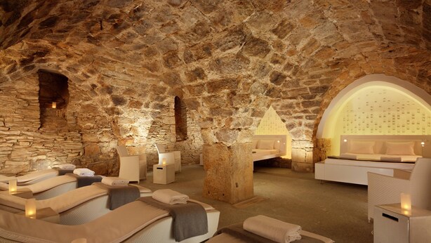 Una habitación con paredes de piedra, camillas de masaje, un mostrador de recepción y una zona de estar.