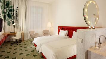 A hotel room with two beds, a desk, a chair, a vanity with a mirror, and a window with curtains.